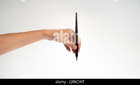 La main gauche femelle tient un stylo calligraphique sur un fond blanc, le geste tombe dans l'inkwell. Photo de haute qualité Banque D'Images