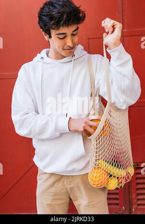 Contenu homme debout dans la rue et de mettre des provisions fraîches dans un sac en filet écologique Banque D'Images