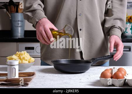 Faites une récolte anonyme en versant de l'huile d'olive dans une poêle tout en préparant une omelette espagnole maison avec des œufs et des pommes de terre hachées sur la table de la cuisine maison Banque D'Images
