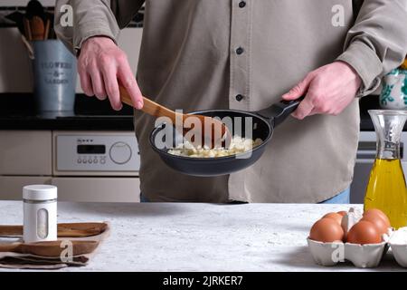 Inreconnaissables crop mâle chef friture oignon dans la poêle tout en cuisant l'omelette espagnole traditionnelle dans la cuisine Banque D'Images