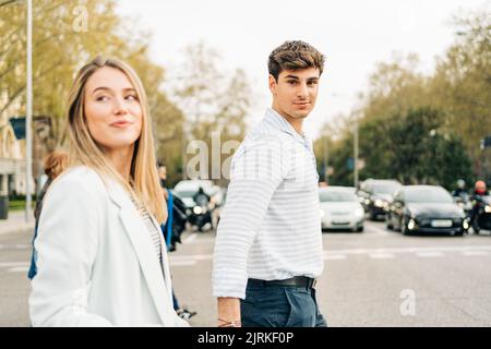Vue latérale du contenu couple élégant tenant les mains et traversant la route tout en marchant dans la ville Banque D'Images