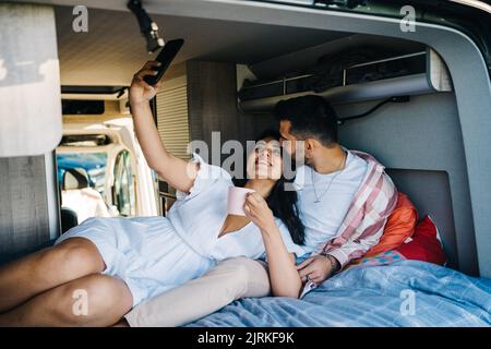 Couple ethnique joyeux de voyageurs allongé sur le lit dans un campeur et prenant auto-portrait-shot sur un smartphone pendant le voyage Banque D'Images
