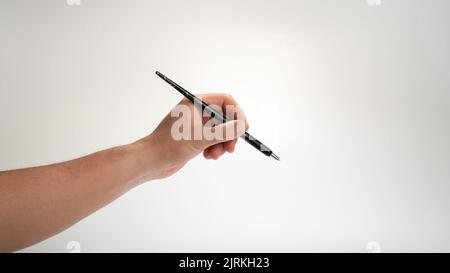 la main gauche des hommes tient un stylo de calligraphie sur un fond blanc, le geste tombe dans l'inkwell. Photo de haute qualité Banque D'Images