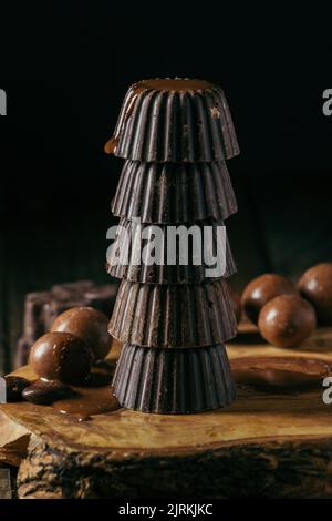 Appétissant pralines au chocolat noir empilées les unes sur les autres et servies sur un panneau de bois sur fond noir Banque D'Images