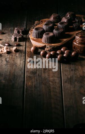 De délicieux chocolats faits main placés sur une planche à découper en bois près d'un pot de mousse dans la cuisine Banque D'Images