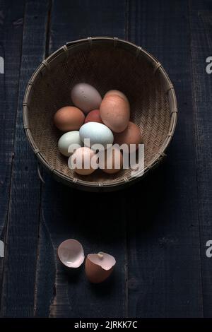 D'en haut, un bol en osier rempli d'œufs crus sur une table en bois avec coquille d'œuf près Banque D'Images