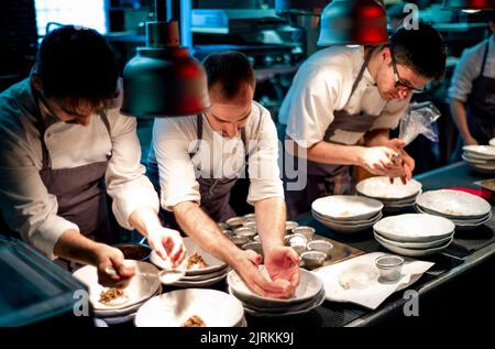 Les jeunes cuisent des hommes dans des tabliers servant avec soin des plats en céramique blanche dans la cuisine du restaurant Banque D'Images