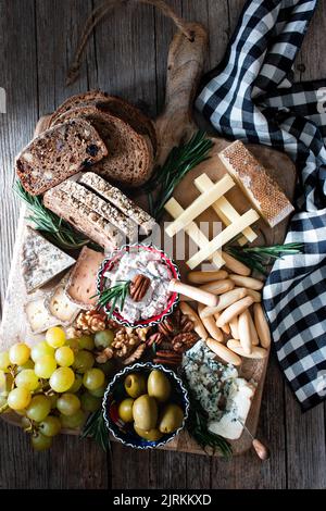 De dessus plusieurs types de fromage avec du pain, des olives et des raisins sur plateau de fromage sur table en bois Banque D'Images