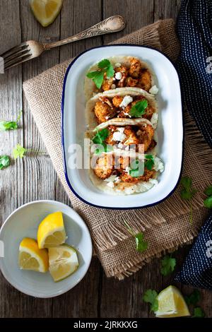 De dessus en-cas de chou-fleur tacos dans un bol et morceaux de citron dans l'assiette sur table en bois Banque D'Images