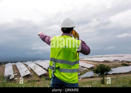 Vue arrière d'un homme méconnu qui parle sur un talkie-walkie contre une centrale solaire et un ciel gris couvert Banque D'Images