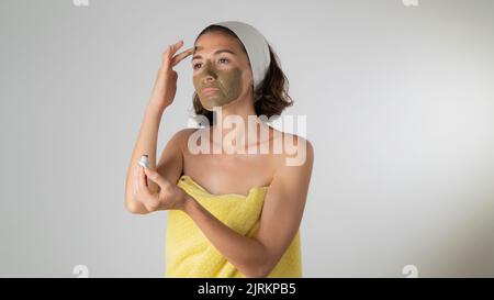 Femme dans une serviette fait un masque de visage - soins à domicile pour la peau du visage. Photo de haute qualité Banque D'Images