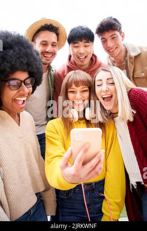 Photo verticale. Groupe multiculturel d'amis utilisant des téléphones cellulaires et riant - les étudiants gaies se sont alignés et regardant l'écran de smartphone. Jeune Banque D'Images