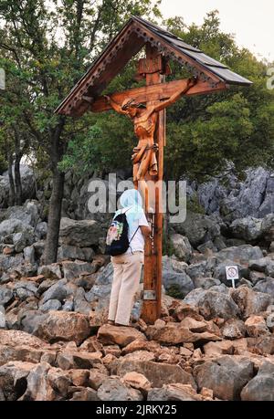 Une femme pèlerine prie devant le crucifix en bois situé sur Podbrdo (colline d'apparition) près de la statue de la Sainte Vierge Marie (Medjugorje) Banque D'Images