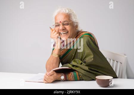 Femme indienne âgée en vêtements traditionnels lisant un livre amusant Banque D'Images