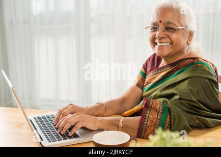 Femme indienne heureuse et âgée travaillant sur un ordinateur portable à la maison Banque D'Images
