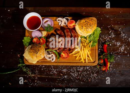 restauration rapide hamburger pommes de terre frites saucisses côtelettes ketchup tomates oignons poivrons champignons sur une planche de bois sur la table vue sur le barbecue mix Banque D'Images