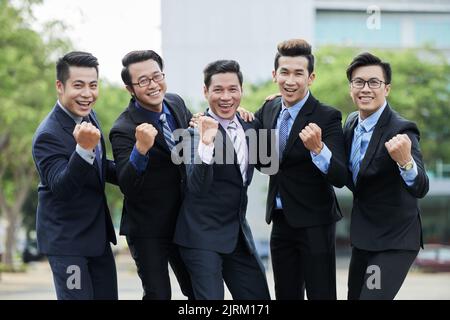 Portrait de groupe d'entrepreneurs asiatiques joyeux portant des costumes élégants, regardant l'appareil photo avec de grands sourires et célébrant la victoire après la fin des négociations productives Banque D'Images