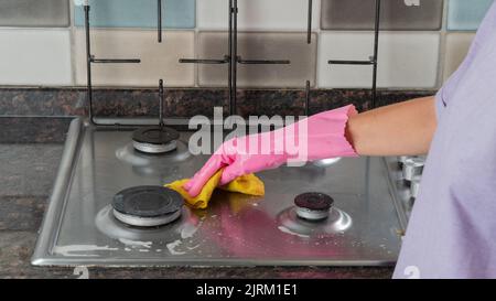 La main gantée d'une femme lave une cuisinière à gaz avec un chiffon Banque D'Images