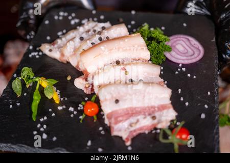 Lard fumé, bacon, un demi-morceau, sur un fond en bois foncé. Vue de dessus, gros plan. Banque D'Images