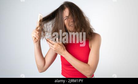 Cela fait mal à une femme en peignant les cheveux coquins et emmêlés - en tirant un peigne et en tirant ses cheveux Banque D'Images