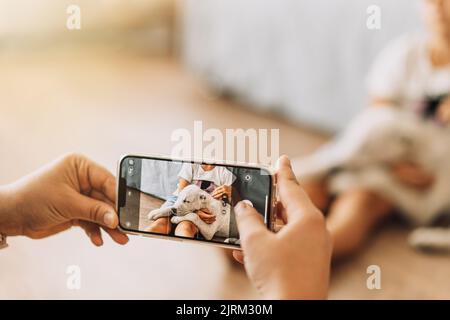 La fille prend une photo au téléphone alors qu'un chiot dort sur les jambes d'un enfant Banque D'Images