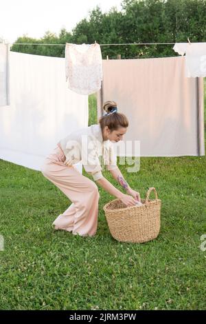 Jour de blanchisserie. Une femme porte du linge et des serviettes sur un arbre dans la cour d'une maison de village. Concept de chalet d'été. Banque D'Images