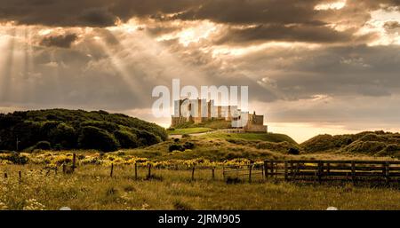 Un cliché spectaculaire du château de Bamburgh avec la lumière du soleil qui se déferle à travers les nuages et qui tombe sur le château Banque D'Images