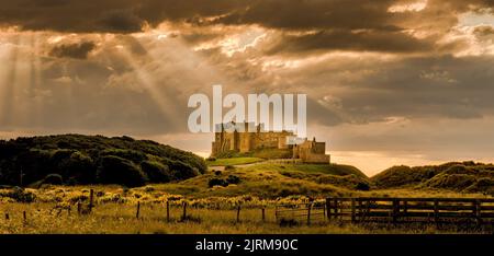 Un cliché spectaculaire du château de Bamburgh avec la lumière du soleil qui se déferle à travers les nuages et qui tombe sur le château Banque D'Images