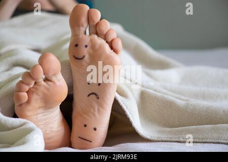 un sourire et des émoticônes tristes sont dessinés sur la jambe de la fille, les jambes sur le lit, les émoticônes drôles sont dessinées sur la jambe, les émotions Banque D'Images