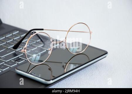 lunettes téléphone et ordinateur portable se trouvent sur la table sur un fond blanc, le travail en ligne et l'éducation Banque D'Images