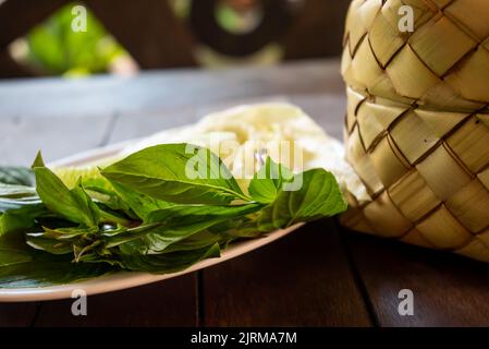 Panier de riz collant en osier de bambou appelé 'Kratip' dans la province du nord-est, en Thaïlande, servi avec un plat d'accompagnement de légumes sur la table en bois. Banque D'Images