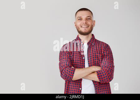 jeune homme souriant posant avec des bras croisés sur fond gris studio Banque D'Images