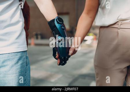 Jeune homme handicapé avec une main artificielle prothétique marchant et tenant la main de petite amie de femme Banque D'Images