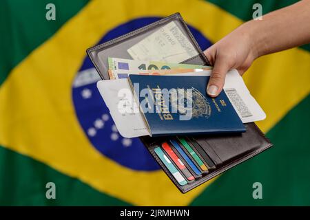 Main tenant le passeport brésilien avec le drapeau brésilien dans le fond flou. Banque D'Images