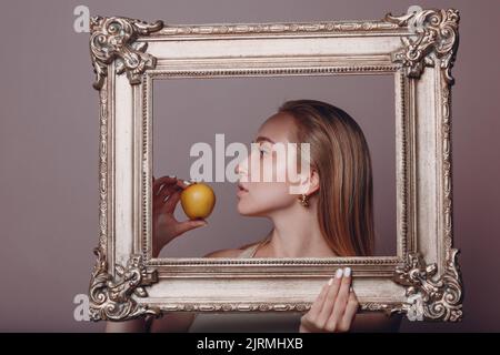 Jeune femme millénial cheveux blonds tient image dorée cadre dans les mains visage portrait avec pomme Banque D'Images
