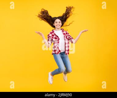 Visage d'adolescent avec des cheveux fous de mouvement. Bonheur, liberté, mouvement et enfant. Jeune fille adolescente sautant dans l'air sur fond jaune. Banque D'Images