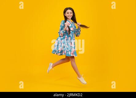 Pleine longueur petite joie ado fille 12, 13, 14 ans saut et mouche isolé sur fond jaune studio. Banque D'Images