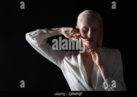 Jeune femme blonde albino faisant la gymnastique faciale automassage et des exercices rajeunissants sur fond noir. Banque D'Images