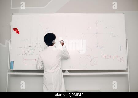 Femme afro-américaine enseignante de mathématiques écrivant sur tableau blanc avec marqueur. Banque D'Images