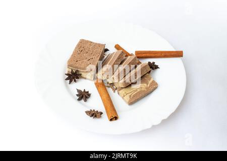 Tranches de halva sur une assiette blanche, avec des graines d'anis et des bâtonnets de cannelle, isolées sur fond blanc Banque D'Images