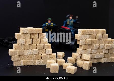 Des policiers en peluche défocused, déchirant un mur en cubes de sucre brun, sur fond noir. Concept soft focus Diet Wars. Banque D'Images