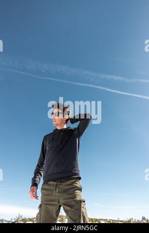 Homme caucasien beau posing avec le ciel bleu dans le fond. Il porte un chandail noir et des lunettes de soleil Banque D'Images