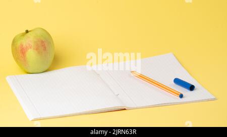 Ouvrez le carnet à carreaux avec un stylo et une pomme sur fond jaune, étudiez Banque D'Images