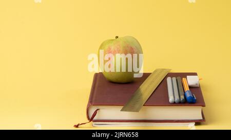 Manuels scolaires, stylos et crayons, une pomme sur fond jaune - retour à l'école Banque D'Images