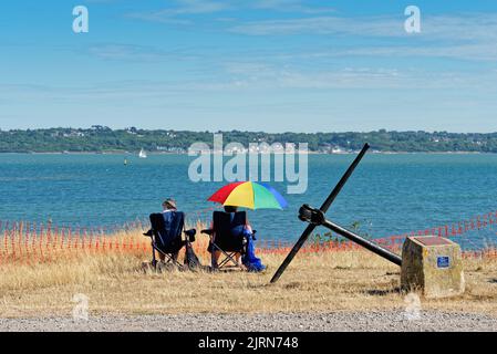 Vue arrière d'un couple de personnes âgées assis sur des chaises et profitant de la vue sur le Solent lors d'une journée d'été au parc régional de Lepe, Hampshire Angleterre Royaume-Uni Banque D'Images