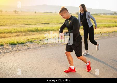 L'image au premier plan montre un jeune garçon sportif qui sourit et regarde la montre sur sa main, et en arrière-plan une jeune femme qui est Banque D'Images