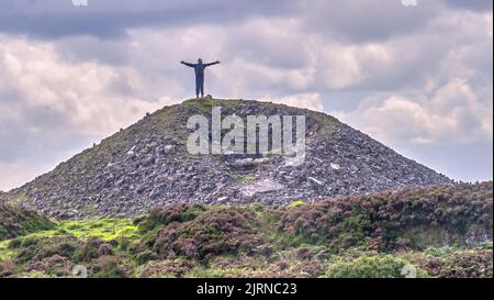 Silhouette d'un homme debout au-dessus d'une montagne avec les bras étirés. Banque D'Images