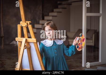 une petite fille mignonne tire derrière un chevalet. rêvant Banque D'Images