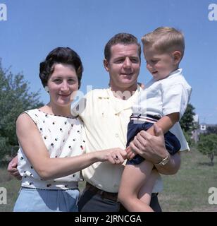 1960s, parents historiques heureux, le père tenant son jeune fils, la mère tient aux doigts du petit garçon, USA. Banque D'Images