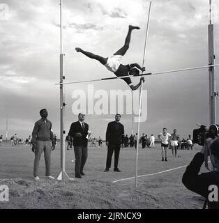 1960s, historique, un caméraman filmant un athlète arabe, un polevaulter, avec sa position de pieds non conventionnels, comme il essaye de dégager la barre, soutenu sur deux montants, Jeddah, Arabie Saoudite. L'un des principaux événements de saut en athlétisme, il s'agit d'un événement de médaille aux Jeux Olympiques depuis 1896. Banque D'Images